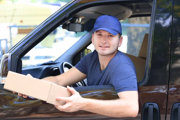 Repartidor masculino joven con caja sentada en coche —  Fotos de Stock