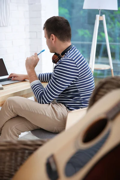 Jeune compositeur assis à un bureau avec un ordinateur portable dans la salle de lumière — Photo