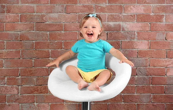 Bebé niña en vestido de color sentado en una silla de bar sobre un fondo de pared de ladrillo — Foto de Stock