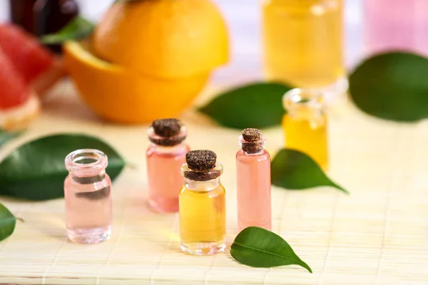 Bottles with essential oil, fruits and leaves on bamboo napkin — Stock Photo, Image