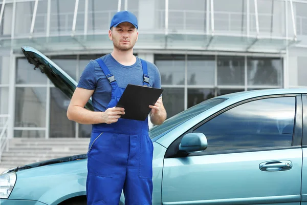 Mechaniker mit Klemmbrett und Stift steht neben Auto — Stockfoto