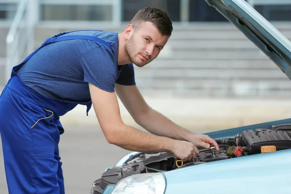 Mechanic standing in front of the open hood and repairing the car — Stock Photo, Image