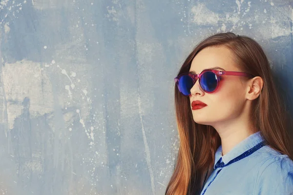 Młoda kobieta stylowe w niebieską koszulę i okulary na szarym tle — Zdjęcie stockowe