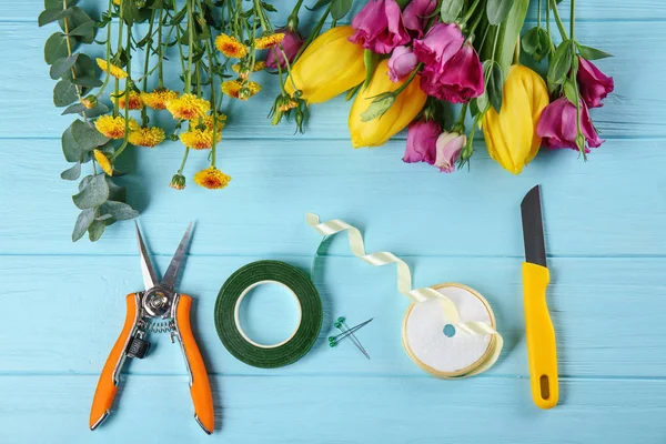 Hermosas flores y equipo de floristería sobre fondo de madera azul — Foto de Stock