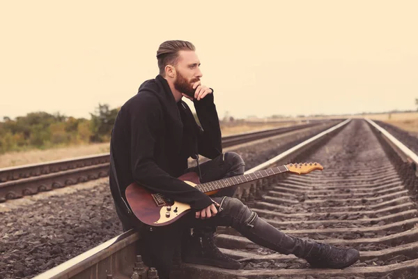 Bonito homem com guitarra sentado na estrada de ferro — Fotografia de Stock