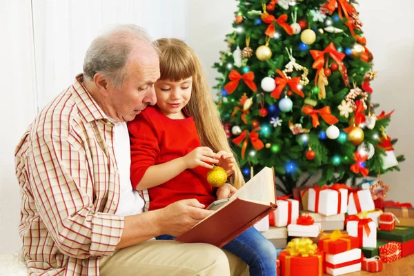 Uomo anziano leggere libro con sua nipote in soggiorno decorato per Natale — Foto Stock