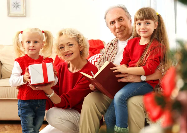 Coppia anziana e le loro nipoti con regalo di Natale e libro in soggiorno — Foto Stock