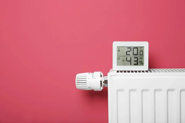 Electronic thermometer on heating battery and pink background — Stock Photo, Image