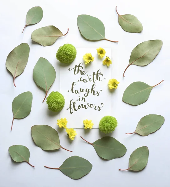 Inscription "THE EARTH LAUGHS IN FLOWERS" written on paper with flowers and leaves on white background — Stock Photo, Image