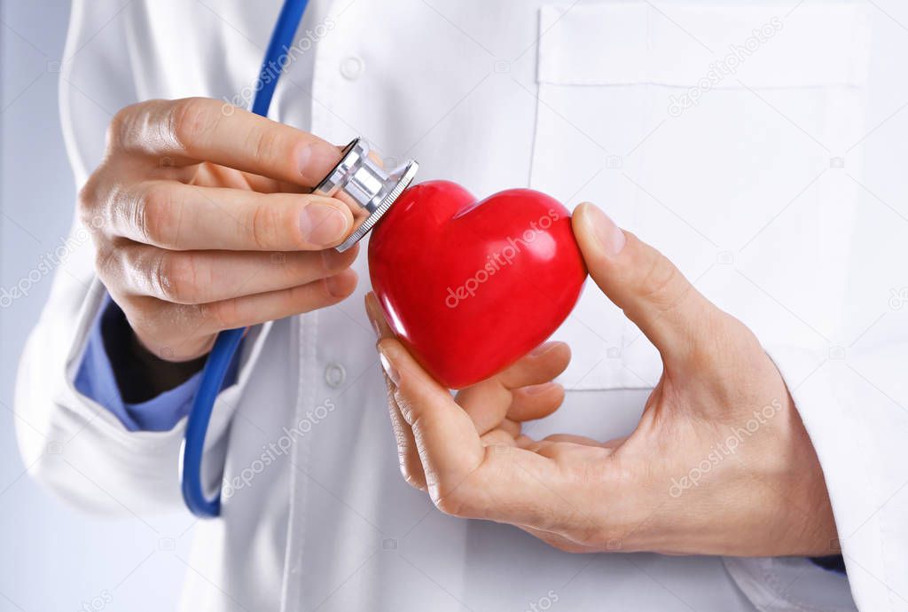Male doctor hands attaching stethoscope to red heart, close up view