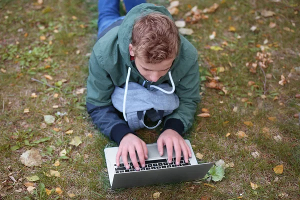 Teenager with laptop lying on lawn in autumn park — Stock Photo, Image