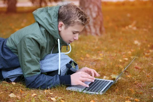 Tiener met laptop liggen op gazon in het najaar park — Stockfoto