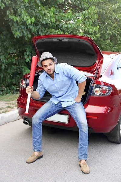 Handsome young man with baseball bat sitting in car trunk — Stock Photo, Image