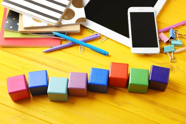 Tablet, copybook and wooden cubes on color background — Stock Photo, Image