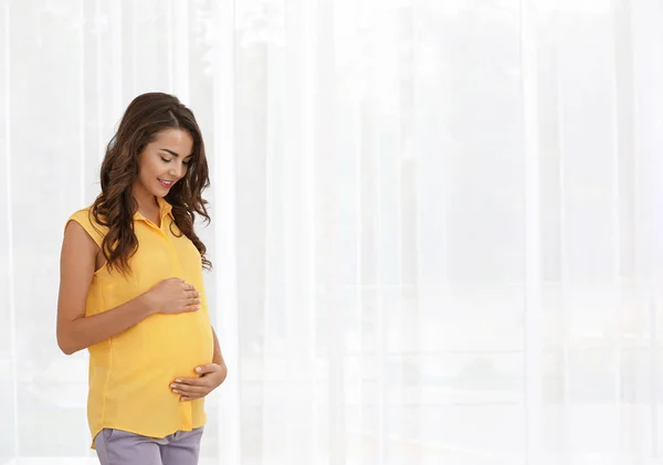 Беременная женщина стоит у окна — стоковое фото