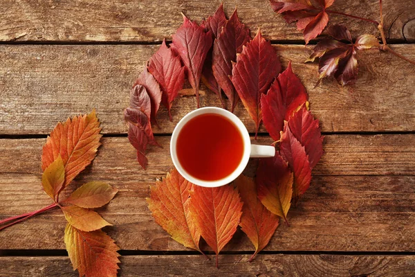 Herbstkomposition mit einer Tasse warmen Tee und bunten Blättern auf Holzgrund — Stockfoto