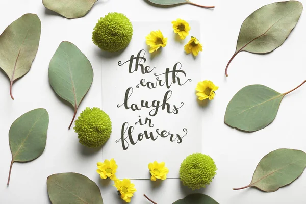 题字"地球笑中花"写在纸上用鲜花和白色背景上的叶子 — 图库照片