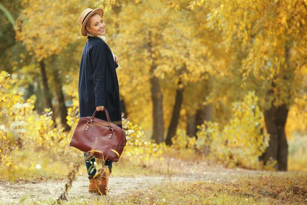 Красивая девушка с кожаной сумкой в осеннем парке — стоковое фото