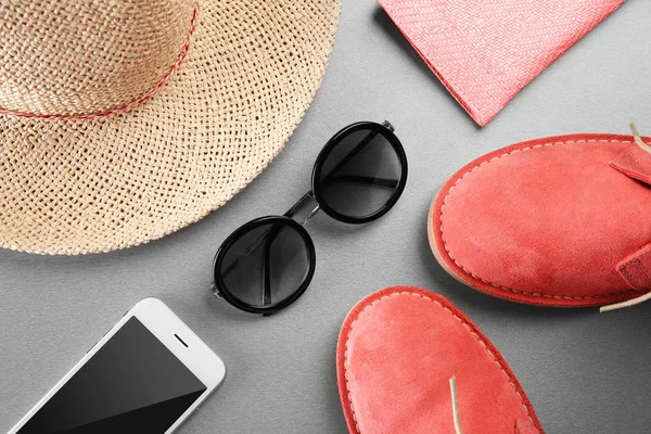 Сонцезахисні окуляри, мобільний телефон та взуття з солом'яним капелюхом на сірому фоні. Концепція продажу — стокове фото