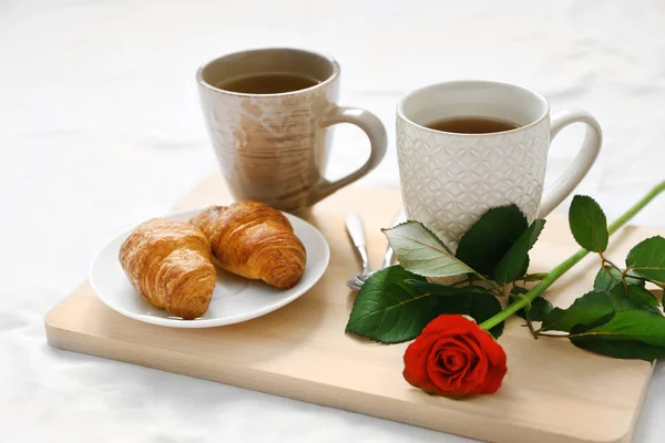 Tazas de té, croissants y rosa en bandeja de madera. Desayuno romántico en la cama — Foto de Stock