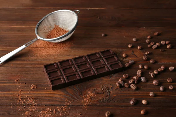 Chocolate with sieve and beans on wooden table — Stock Photo, Image