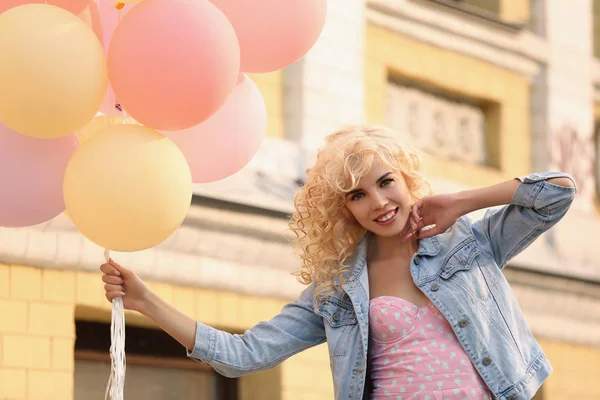 Beautiful young woman holding air balloons on street — Stock Photo, Image