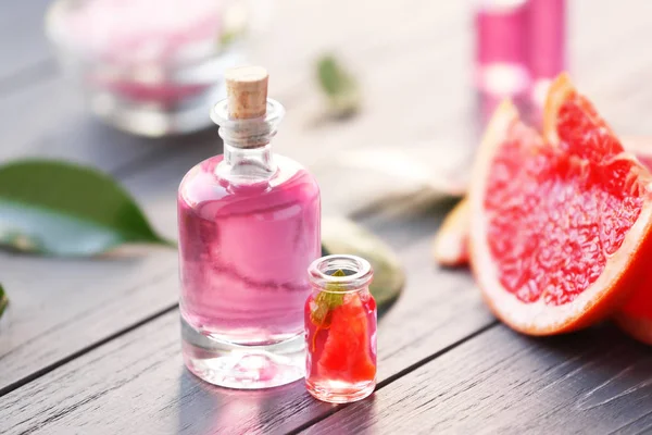 Botellas con rebanadas de aceite esencial y pomelo sobre mesa de madera —  Fotos de Stock