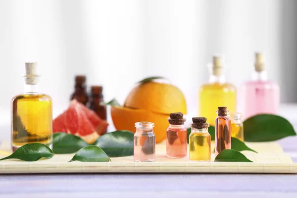Bottles with essential oil, fruits and leaves on bamboo napkin — Stock Photo, Image