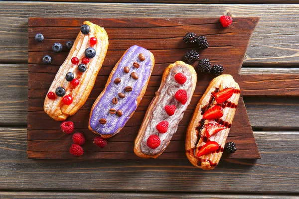 Délicieuses éclairs colorés aux baies sur planche à découper en bois — Photo