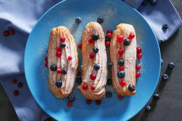 Смачні еклери з ягодами на блакитній тарілці — стокове фото