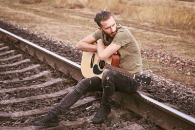 Demiryolu üzerinde oturan gitar ile yakışıklı adam