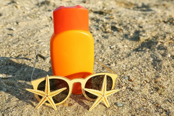 Sunscreen cream, sunglasses and starfish on sea coast — Stock Photo, Image