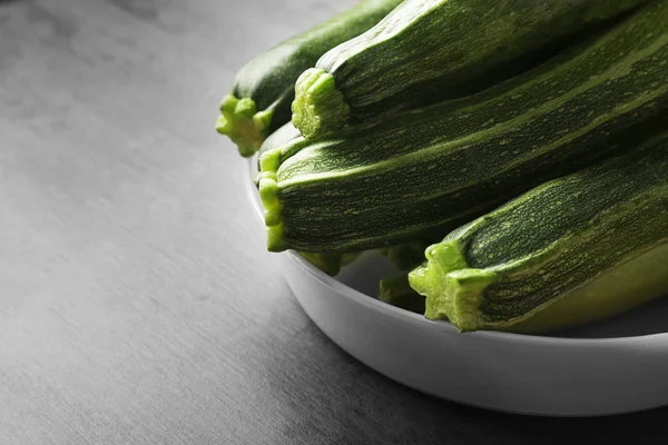 Bowl with fresh green zucchini on color background