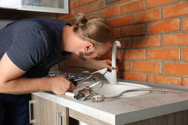 Handsome plumber replacing faucet in kitchen, close up view — Stock Photo, Image