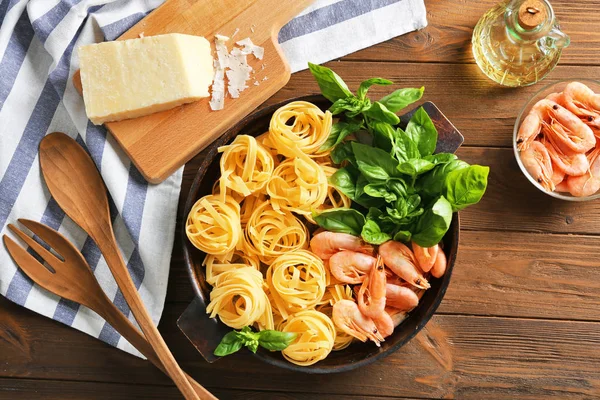 Pfanne mit Zutaten für leckere Pasta, Gabel, Löffel, Serviette und Küchenbrett auf Holztisch, Draufsicht — Stockfoto