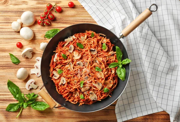 Sartén con sabrosa pasta, servilleta y productos en mesa de madera — Foto de Stock