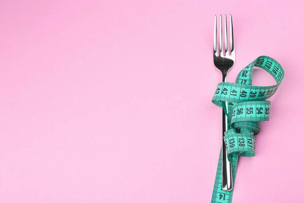 Измерительная лента, обернутая вокруг вилки, лежащей на цветной поверхности. Концепция питания
