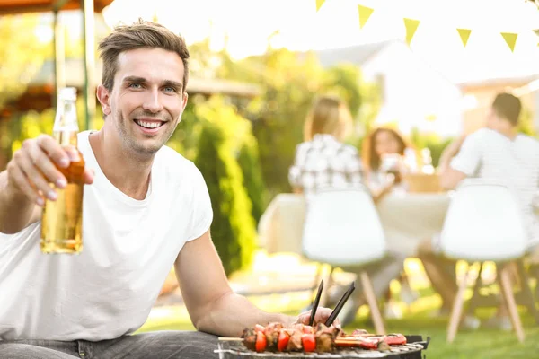 Young man with bottle of beer preparing barbecue — Stock Photo, Image