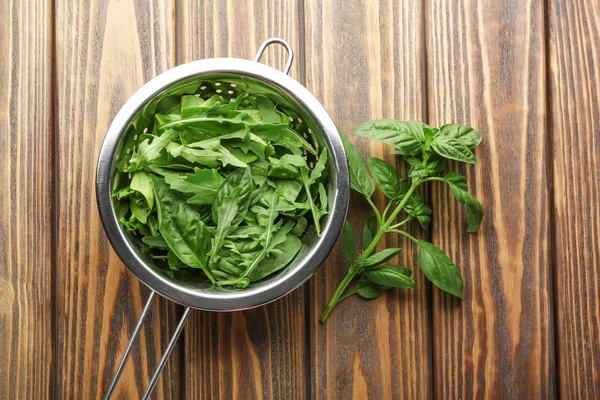 Arugula com manjericão em escorredor sobre mesa de madeira — Fotografia de Stock