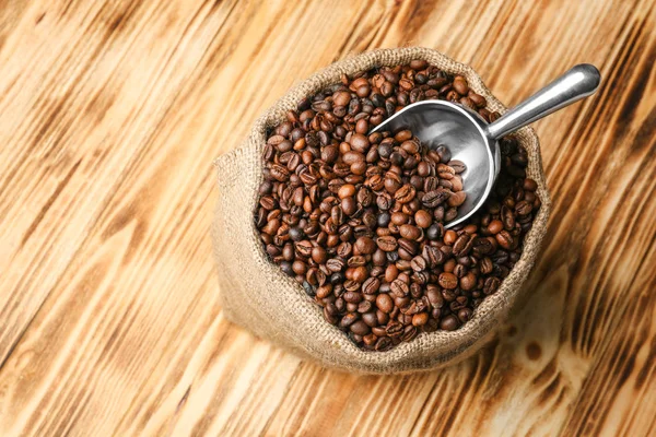 Sack with coffee beans and scoop on wooden background — Stock Photo, Image