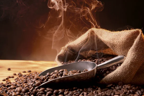 Ziarna kawy, worek i czerpak na drewnianym stole na ciemnym tle, zbliżenie — Zdjęcie stockowe