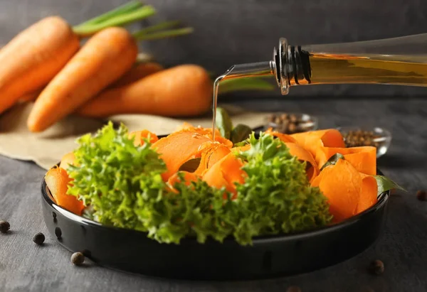 Добавление оливкового масла к нарезанной морковке и салату на тарелке — стоковое фото