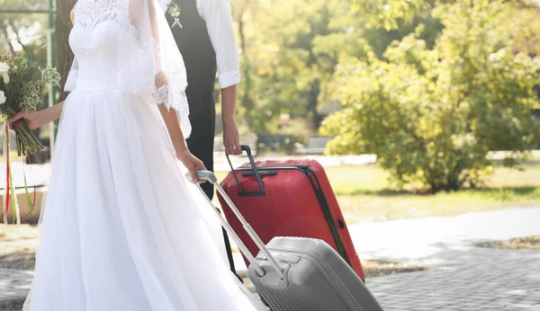 Жених и невеста с большими чемоданами выходят на улицу — стоковое фото
