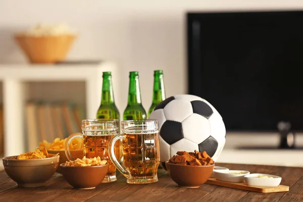 Leckere Snacks, Bier und Ball auf Küchentisch vor verschwommenem Hintergrund — Stockfoto