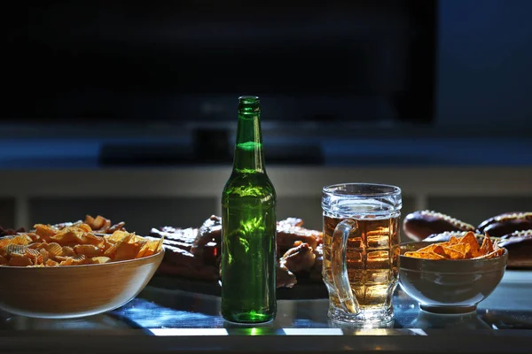 Petiscos saborosos e cerveja na mesa da cozinha contra fundo desfocado — Fotografia de Stock