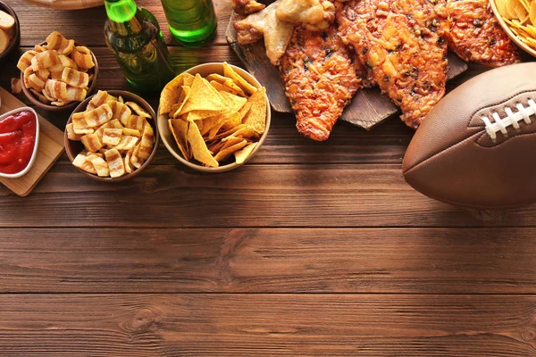 Tasty snacks and rugby ball on wooden table — Stock Photo, Image