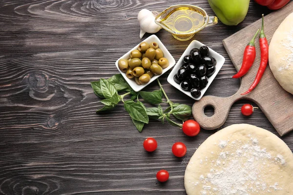 Сырое тесто для пиццы с ингредиентами на деревянном столе — стоковое фото
