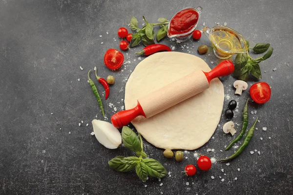 Pasta cruda per pizza con ingredienti in tavola — Foto Stock