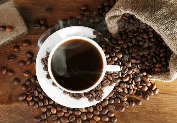 Kopje verse koffie en zak met bonen op houten achtergrond, bovenaanzicht — Stockfoto