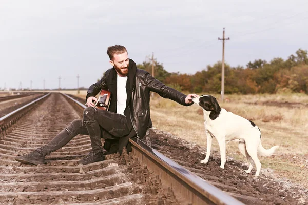 Schöner Mann mit Gitarre und süßem Hund auf der Eisenbahn — Stockfoto